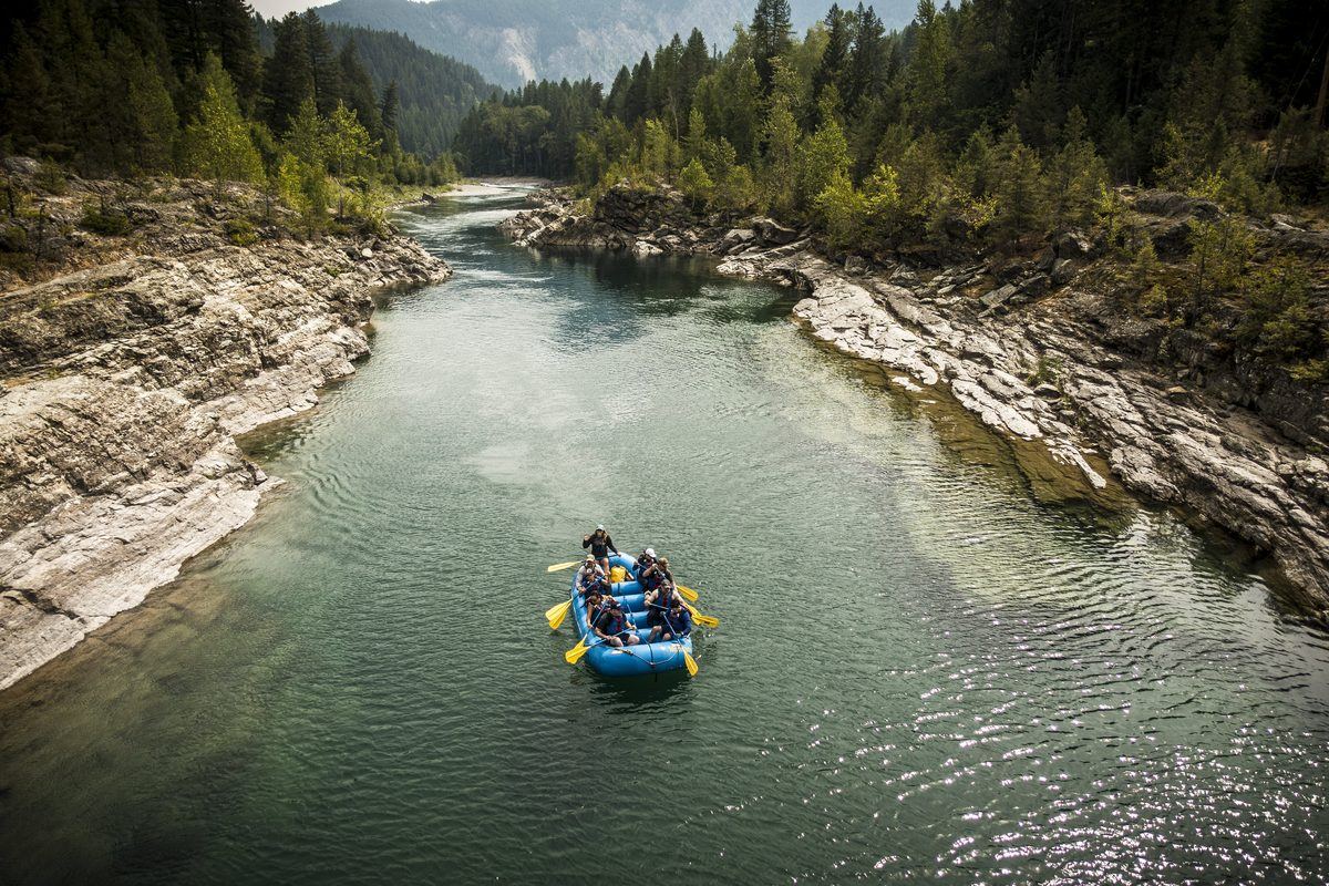 A blue raft of paddlers on the clear green Middle Fork of the Flathead River