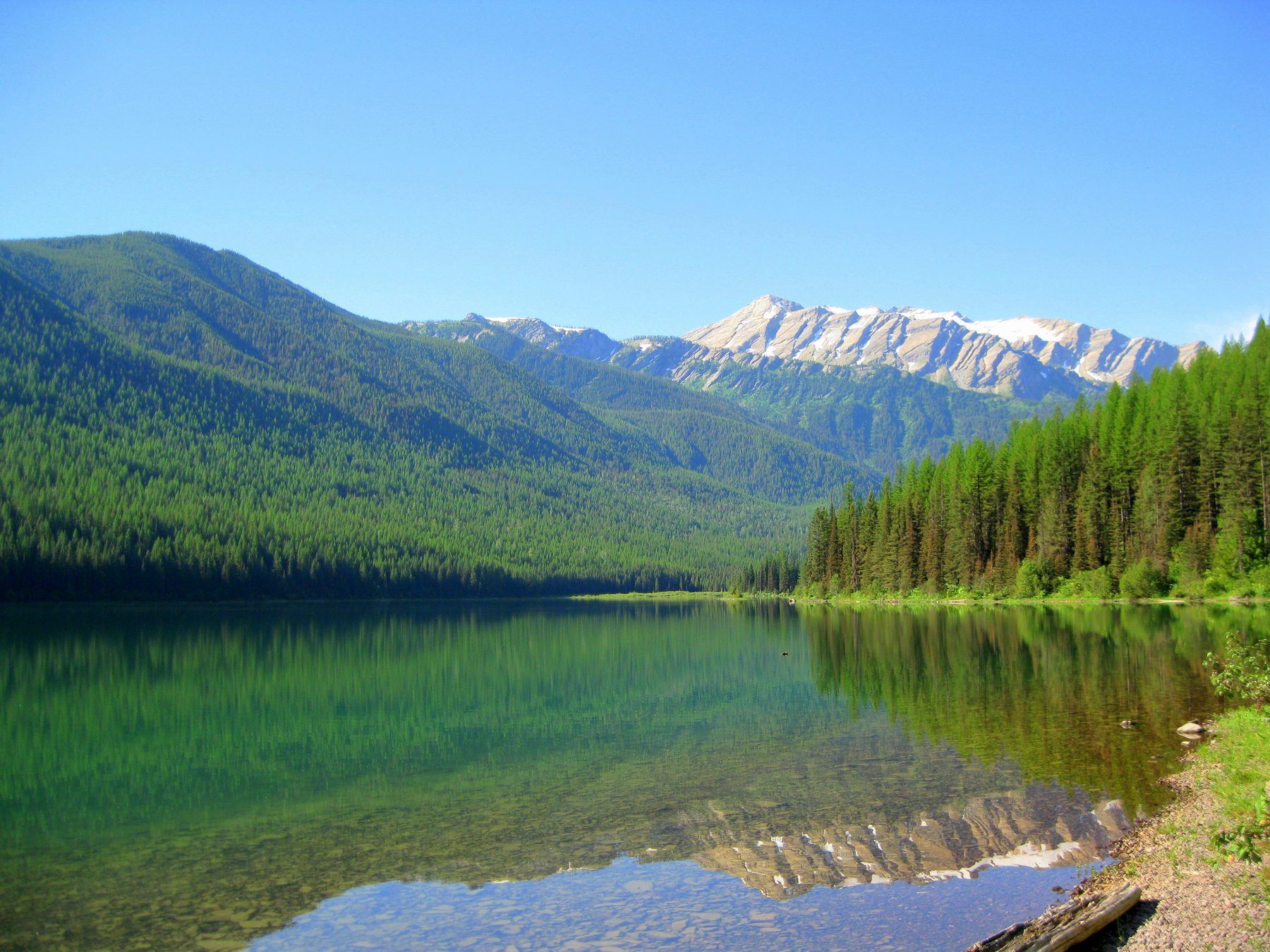 Stanton Lake, clear and green, reflecting forested slopes and Great Northern Mountain